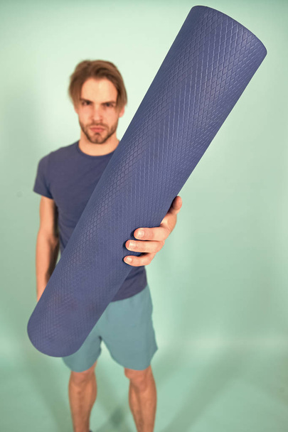 Yoga or pilates mat in hand of blur man. Blue mat rolled in hand. Gym equipment for training and workout. Yoga or pilates and sport activity - Photo, image