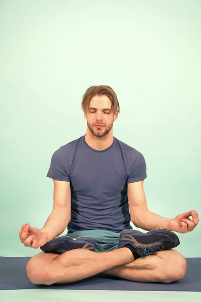 Man meditate on yoga mat. Sportsman relax in lotus pose. Fashion athlete practice yoga in gym. Meditation for body and mind health. Meditation or zen and peace concept - Фото, изображение