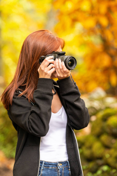 eine junge Frau mit rötlichem Haar fotografiert mit einer Spiegelreflexkamera im Wald  - Foto, Bild