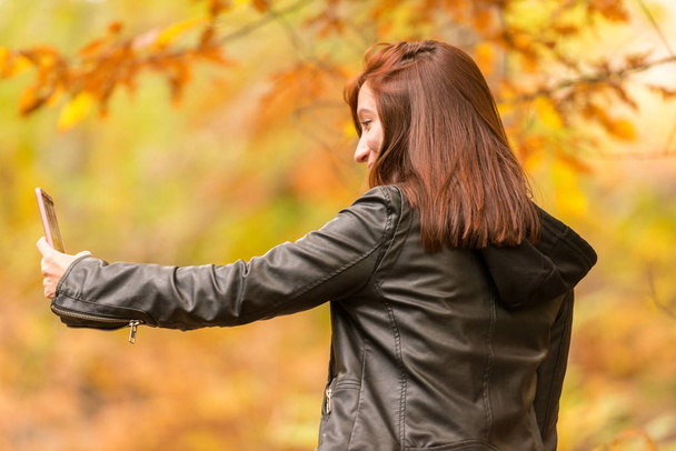 Nuori nainen punertava tukka tekee selfietä hänen matkapuhelin metsässä
 - Valokuva, kuva