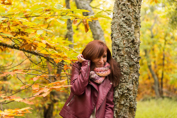 Mujer joven con el pelo rojizo perturbado por las ramas de un árbol en un bosque otoñal
 - Foto, Imagen