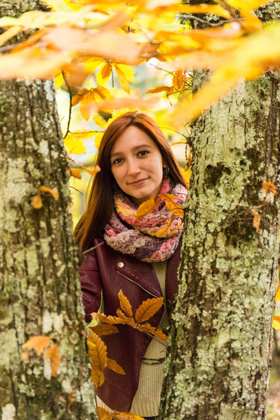 Nuoren punertavan naisen muotokuva syksyisen metsän runkojen joukossa
 - Valokuva, kuva