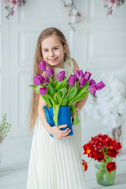 Portrait of a beautiful blue-eyed child, a little girl with a bouquet of tulips in a bright room. Spring Holidays, Mother's Day, Women's Day, Easter. - Foto, afbeelding
