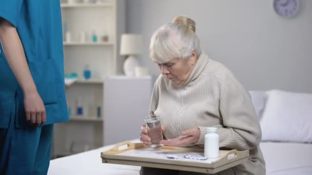 Elderly female patient spilling water on tray while taking pills, bad service - Felvétel, videó