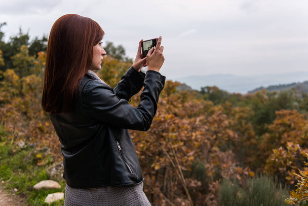 eine junge rothaarige Frau fotografiert mit ihrem Handy im Wald - Foto, Bild