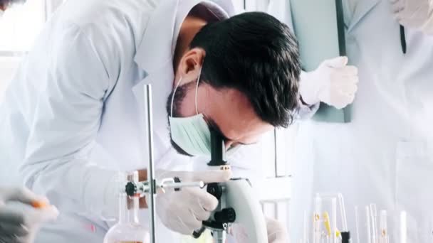 Group of chemists working in a lab. Young white male and female chemists with senior caucasian chemist working together in lab, looking into microscope, close up shot. Science concept. - Video