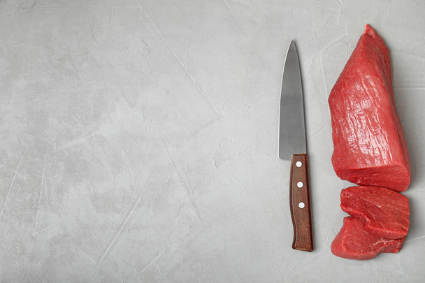 Flat lay composition with raw meat, knife and space for text on grey background - 写真・画像