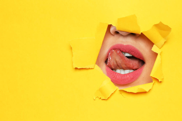 Lips of young woman with beautiful lipstick visible through hole in color paper. Space for text - Foto, Bild