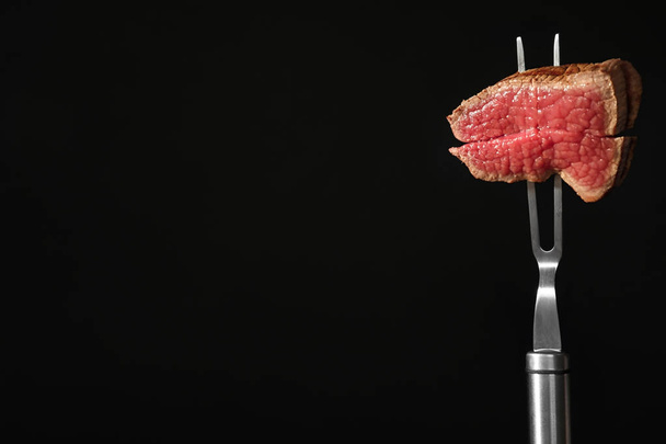 Carving fork with pieces of steak and space for text on black background. Tasty meat - Φωτογραφία, εικόνα