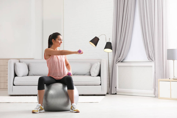 Young woman doing exercise with dumbbells on fitness ball at home. Space for text - Foto, Bild