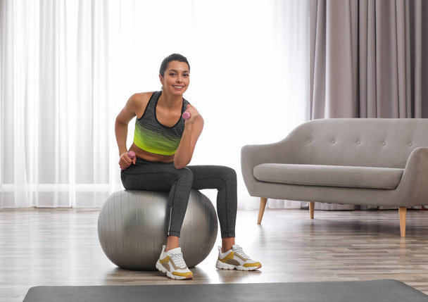 Young woman doing exercise with dumbbells on fitness ball at home. Space for text - Fotografie, Obrázek