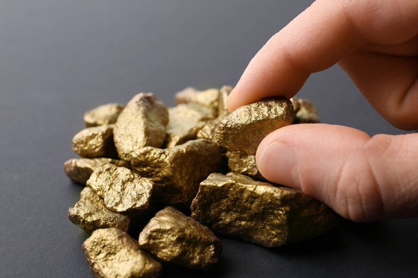 Man taking gold nugget from pile on dark background, closeup - 写真・画像