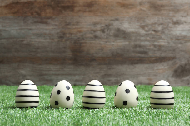 Line of traditional Easter eggs decorated with black paint on green lawn against wooden background, space for text - Foto, afbeelding