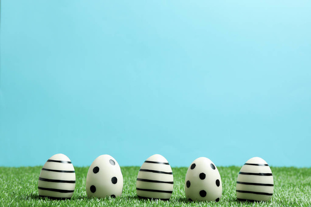 Line of traditional Easter eggs decorated with black paint on green lawn against color background, space for text - Fotografie, Obrázek