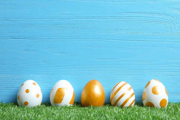 Line of traditional Easter eggs decorated with golden paint on green lawn near wooden wall, space for text - Fotó, kép