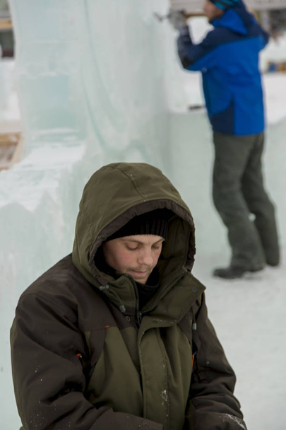 Ritratto di un operaio in giacca verde con cappuccio impegnato nella sistemazione di una città di ghiaccio
 - Foto, immagini