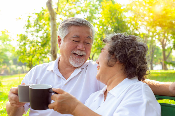 Happy life and long lived concept. Older couple is clinking cup of coffee and enjoying the drink in the morning. Handsome grandfather and beautiful grandmother are laughing and get happiness of life - Photo, Image