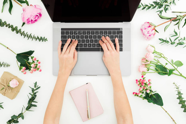 Donna che digita sul portatile. Spazio di lavoro con fiori femminili, portatili, notebook e rosa su sfondo bianco. Vista dall'alto. Posa piatta
. - Foto, immagini