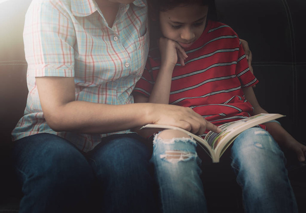 Äiti ja tytär lukevat kirjaa ja pitävät hauskaa viettäessään aikaa kotona lämpimässä valossa.
. - Valokuva, kuva