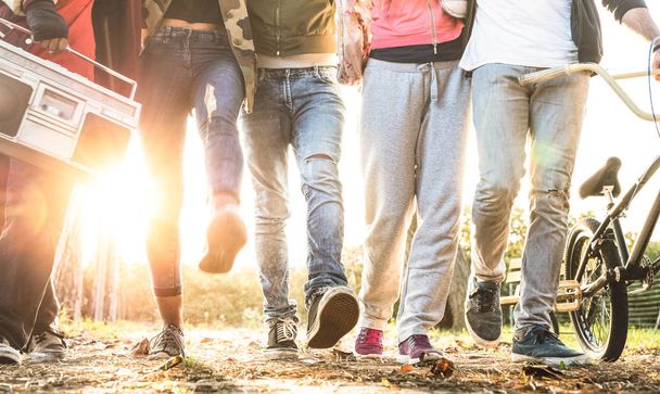 Przyjaciele spaceru w parku miejskiego z podświetleniem i sunflare halo - koncepcja Millenial przyjaźni i wielorasowe młodych ludzi na mody alternatywnej, wspólna zabawa - noga widok z miękkiego ruchu niewyraźne - Zdjęcie, obraz