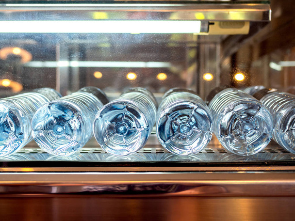 Pohled zdola detail minerální čerstvou pitnou vodou lahví v lednici s neon světlem v kavárně. - Fotografie, Obrázek