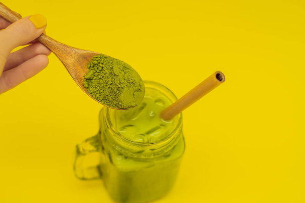Green tea latte with ice in mason jar and straw and spoon with powder matcha on yellow background. Homemade Iced Matcha Latte Tea with Milk zero waste - Photo, image