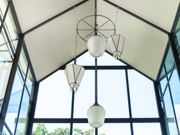 Lámparas modernas colgantes blancas decoradas bajo el techo alto en la cafetería de la casa de cristal
. - Foto, imagen