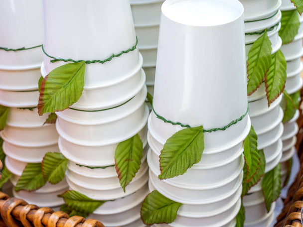 Wit wegwerp kopjes ondersteboven. Stapels van Witboek cups decoratie met groene bladeren in mand. - Foto, afbeelding