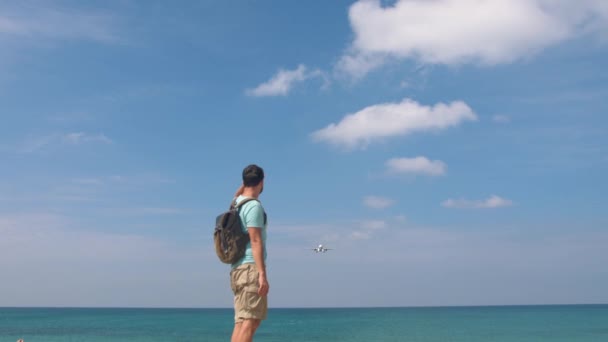Touristenmann mit Rucksack begrüßt Flugzeug zum Reisen. Hallo Urlaubskonzept - Filmmaterial, Video