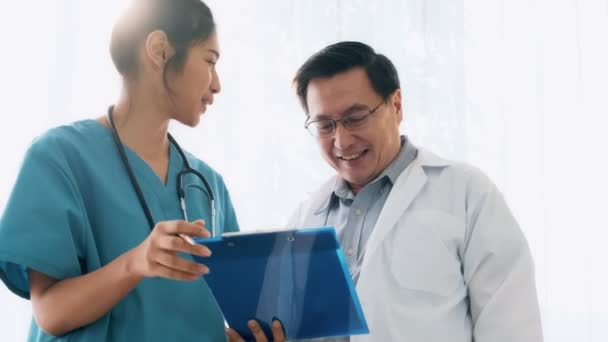 Senior asian man medical doctor standing, talking to young medical woman doctor examine her notes. Young medical doctor career concept. - Footage, Video