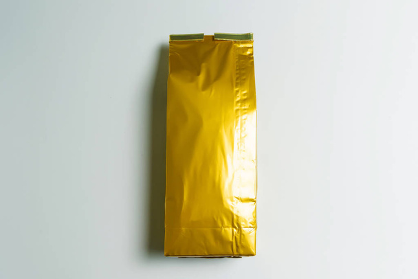 Una bolsa de té de color dorado sobre un fondo blanco. Almacenamiento de té de hoja. Producto natural. Té verde ponderado. Embalaje y clasificación
. - Foto, Imagen