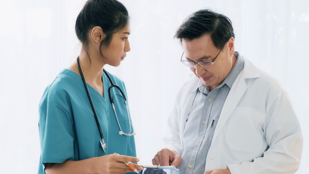 Senior asian man medical doctor standing, talking to young medical woman doctor examine her notes. Young medical doctor career concept. - Footage, Video