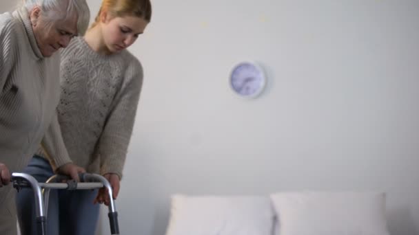 Woman helping grandmother use walking frame rehabilitation after joint surgery - Video