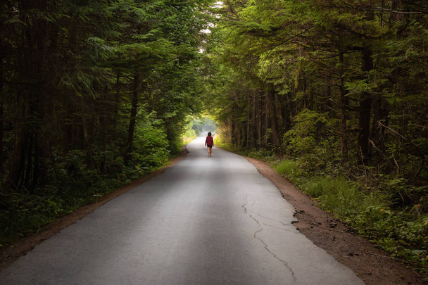 Γυναίκα που περπατά στο δρόμο γραφικό δάσος κατά τη διάρκεια μια έντονη καλοκαιρινή μέρα. Λαμβάνονται σε Florencia Bay, κοντά στο Ucluelet και Tofino, νησί Vancouver, Bc, Καναδάς. - Φωτογραφία, εικόνα
