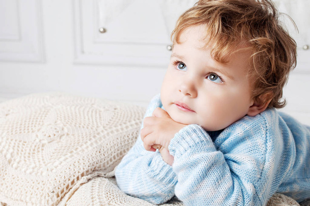 Portrait of happy adorable baby boy on the bed in his room. Thoughtful look up. Copy space - Фото, изображение