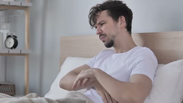 Κουρασμένος νέος άνθρωπος με αυχεναλγία που κάθεται στο κρεβάτι - Πλάνα, βίντεο