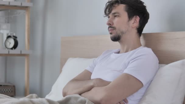 Κουρασμένος νέος Casual με πονοκέφαλο που κάθεται στο κρεβάτι - Πλάνα, βίντεο
