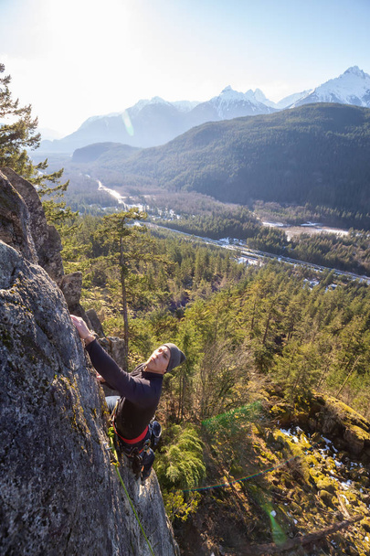 Mannelijke Rock klimmer klimmen op de rand van de klif tijdens een zonsondergang in de zonnige winter. Genomen in gebied 44 in de buurt van Squamish en Whistler, noorden van Vancouver, Bc, Canada. - Foto, afbeelding