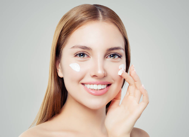 Healthy woman face. Cute girl with clear skin applying cream and smiling. Skincare, beauty and facial treatment concept - Foto, imagen