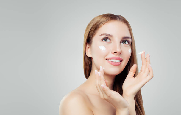 Young happy woman with healthy skin applying cosmetic cream. Skincare, beauty and facial treatment concept - Fotó, kép