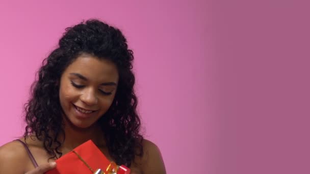 Afro-American woman holding giftbox and looking up, dreaming about romantic date - Кадри, відео