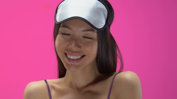 Beautiful Asian woman in pajamas and sleeping mask flirting, looking into camera - Filmati, video