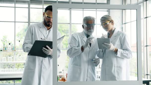 Group of chemists working in a lab. Young white male and female chemists with senior caucasian chemist working together in lab, writing on glass display. Science concept. - Video, Çekim