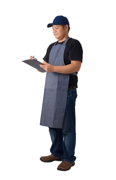 Полный портрет доставщика в черной рубашке и фартуке с буфером для проверки продуктов изолированы на белом фоне с вырезкой пути
 - Фото, изображение