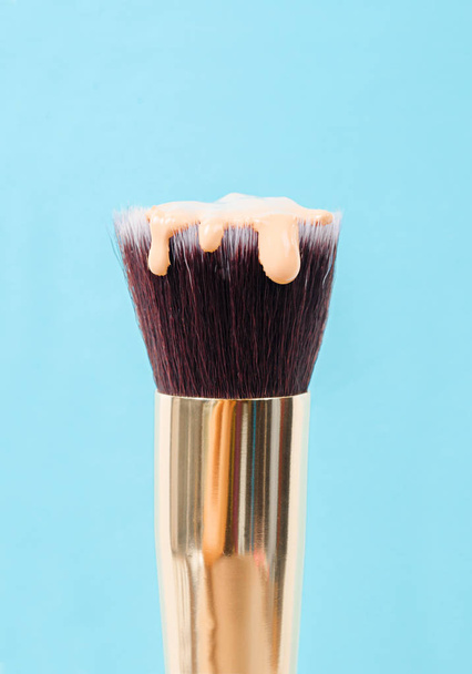 pouring liquid beige makeup foundation on a brush makeup with blue background. - Фото, зображення