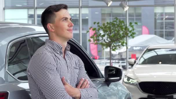 Przystojny mężczyzna uśmiechający się sennie, opierając się na nowy samochód na dealerskiej - Materiał filmowy, wideo