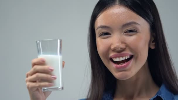 Sorridente ragazza asiatica mostrando vetro di latte in macchina fotografica, concetto di nutrizione sana
 - Filmati, video