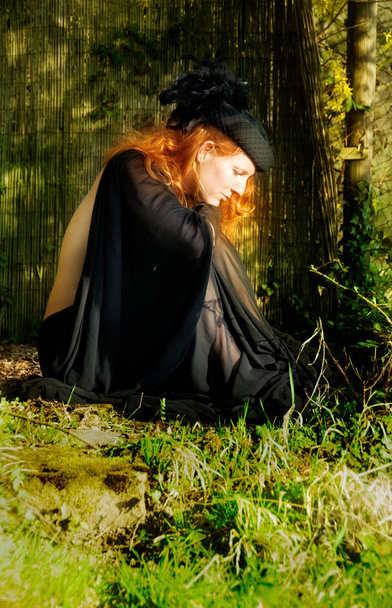 hermosa joven abandonada mujer, en vestido negro con sombrero, se sienta con impaciencia en el parque del jardín de primavera
 - Foto, imagen