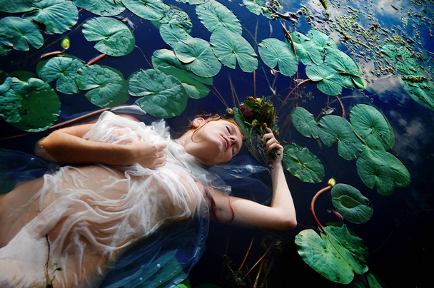 目を閉じて、湖の水で死んでいる白いドレスの花にある赤巻き毛を持つ若いセクシーな不幸な女オフィーリア - 写真・画像