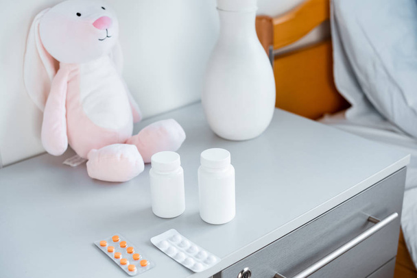 γκρο πλαν θέα βάζο, δοχεία με χάπια και το παιχνίδι στο τραπέζι σε δωμάτιο του νοσοκομείου - Φωτογραφία, εικόνα